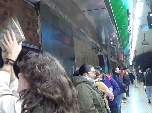 La Muriel apretant la planxa de fang a l'estació mentres la gent mira